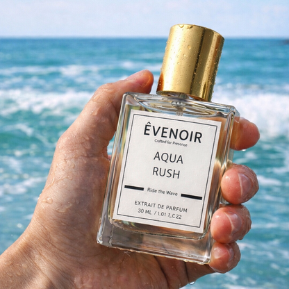 Hand holding Aqua Rush perfume bottle with gold cap, ocean waves in the background